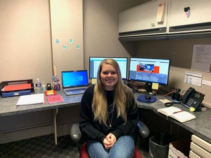 A young woman in an office smiles at the camera.