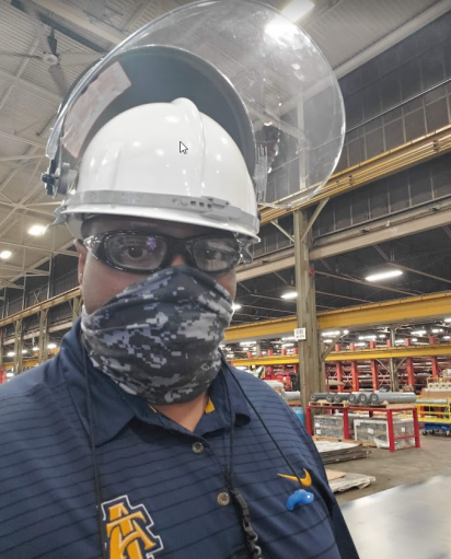 A man wearing a hardhat with face shield, safety glasses and a gaiter looks at the camera.